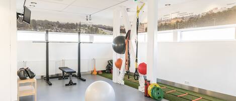 A gym with exercise equipment, a large exercise ball, and a view of the city through large windows.