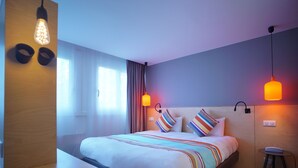 A modern hotel room with a large bed, bedside tables, and a small desk.