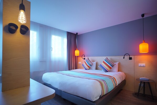 A modern hotel room with a large bed, bedside tables, and a small desk.