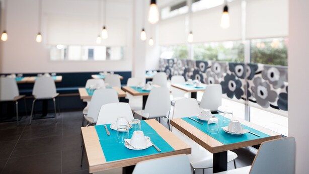A modern dining area with tables and chairs, large windows, and hanging lights.