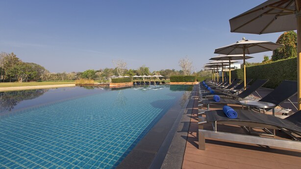 A swimming pool with lounge chairs and umbrellas, surrounded by greenery. - Le Meridien Chiang Rai Resort, Thailand (Chiang Rai)