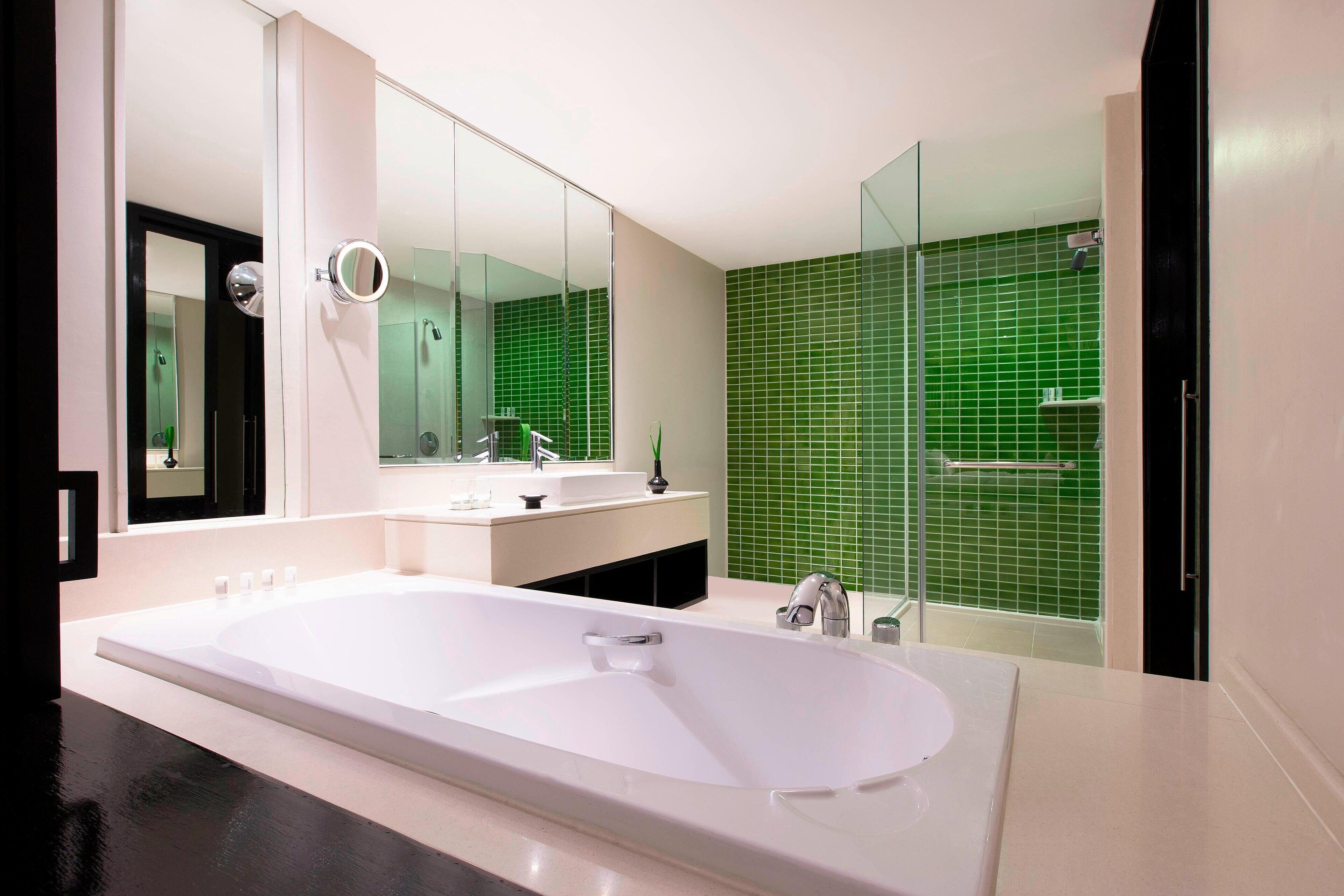 Um banheiro moderno com uma banheira grande, um espelho sobre a pia e um chuveiro com azulejos verdes.