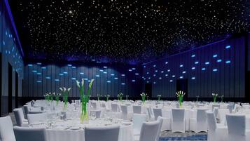 Un salón de banquetes con mesas redondas dispuestas para comer, sillas blancas y altos arreglos florales.