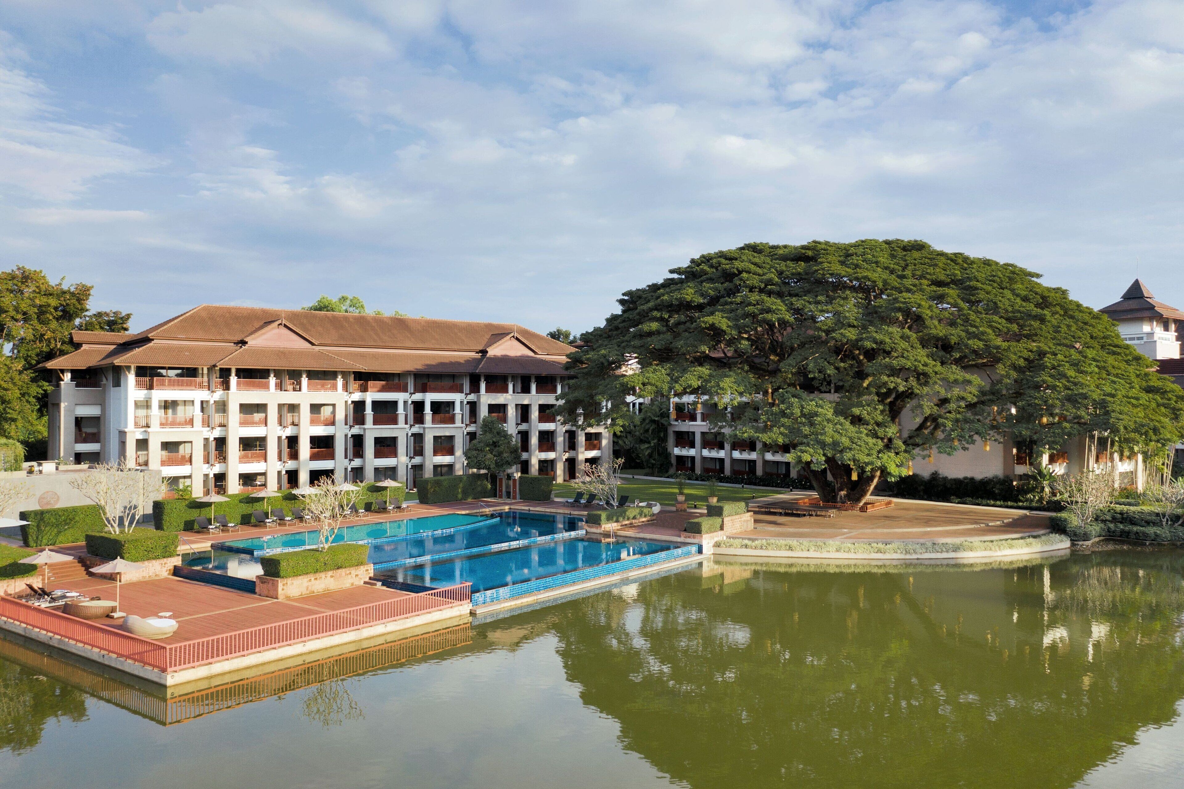 A hotel with a large swimming pool, multiple balconies, and lush greenery.