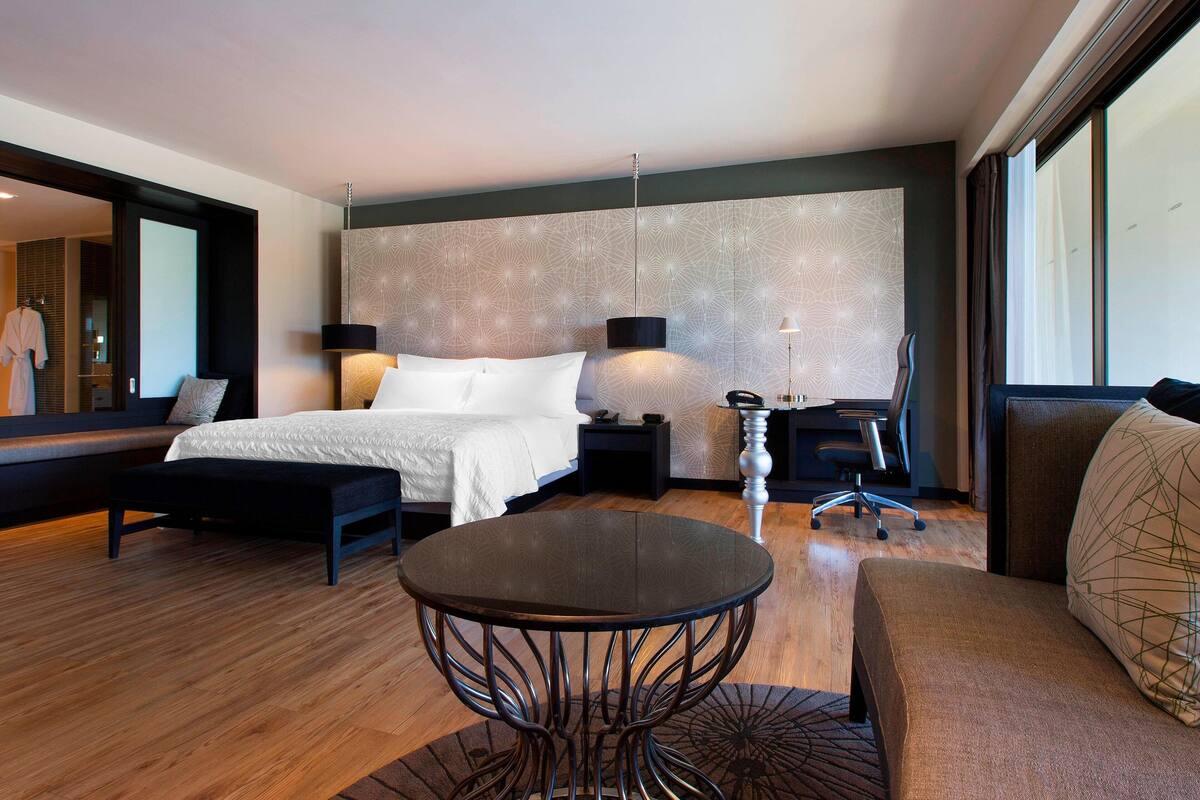 Une chambre d’hôtel moderne avec un grand lit, une table ronde, un canapé et un bureau avec une chaise.