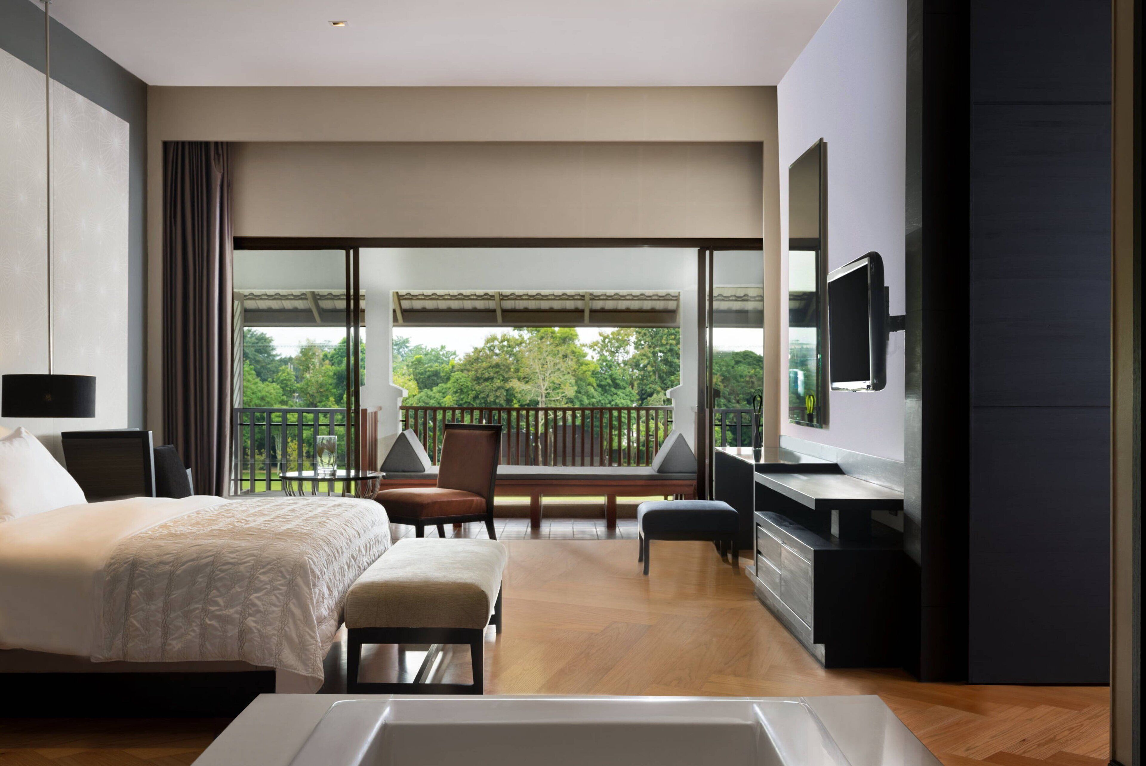 Une chambre d’hôtel moderne, dotée d’un grand lit, d’un bureau, d’une chaise, d’une télévision et d’un balcon offrant une vue sur la verdure.