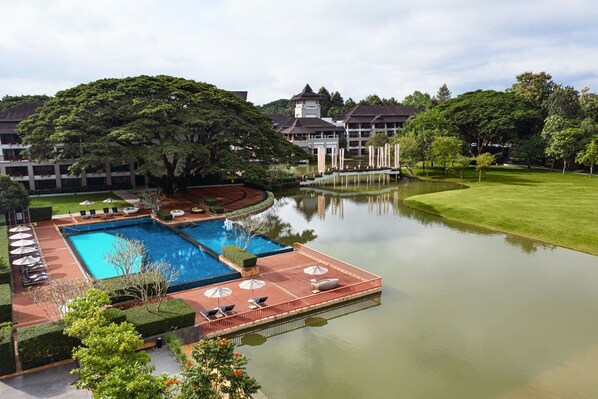 A hotel with a swimming pool, a tennis court, and a large lawn.