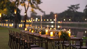 Una larga mesa de comedor al aire libre con velas, sillas y arreglos florales.