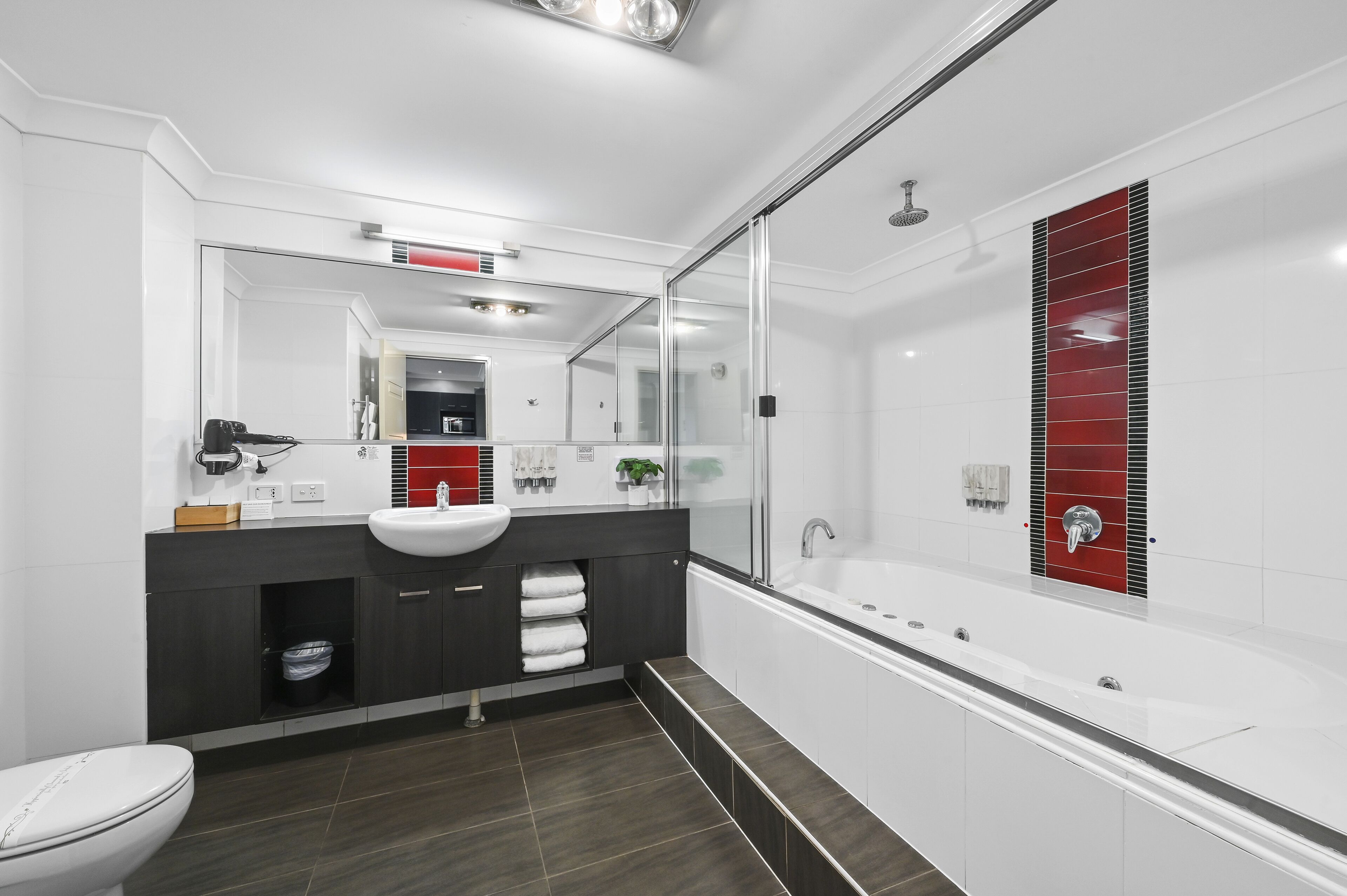 A modern bathroom with a large mirror, white sink, dark cabinetry, and a glass-enclosed shower area.
