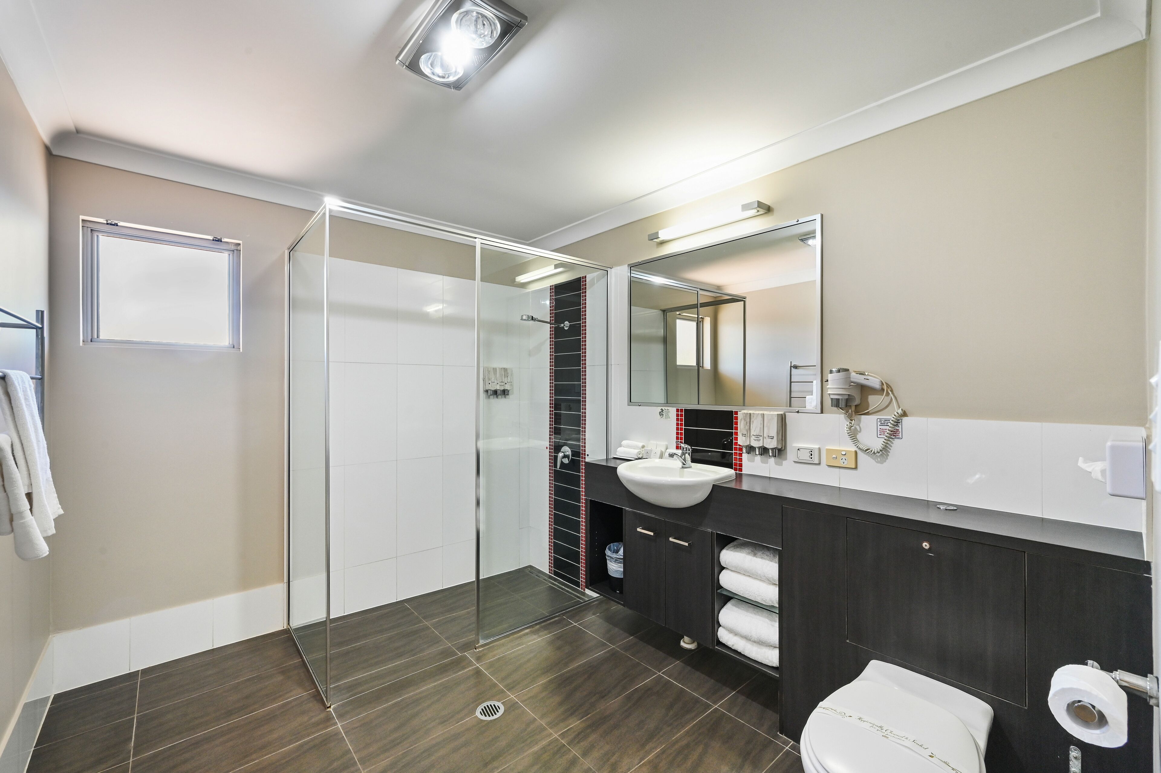 Un baño moderno con cabina de ducha de vidrio, lavabo blanco y tocador oscuro.