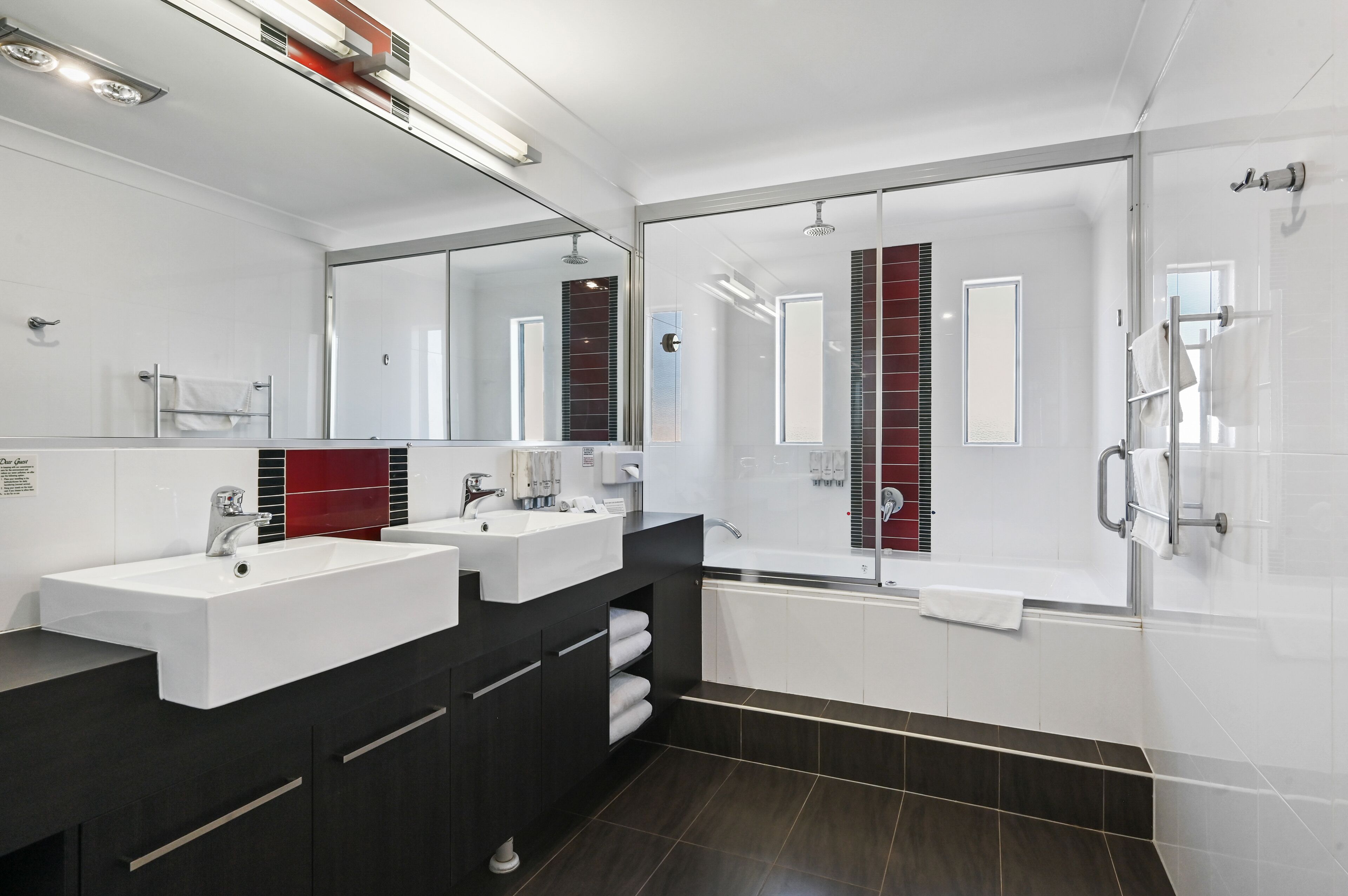 Een moderne badkamer met twee wastafels, een grote spiegel en een douche met glazen wanden.