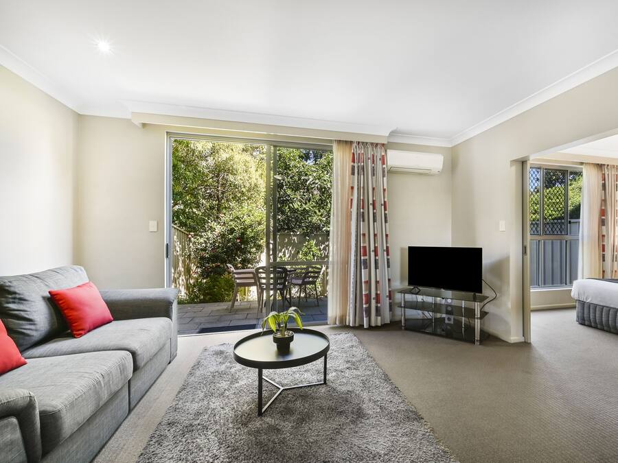 A modern living room with a grey sofa, a coffee table with a plant, a flat-screen TV, and a balcony with a sliding door.