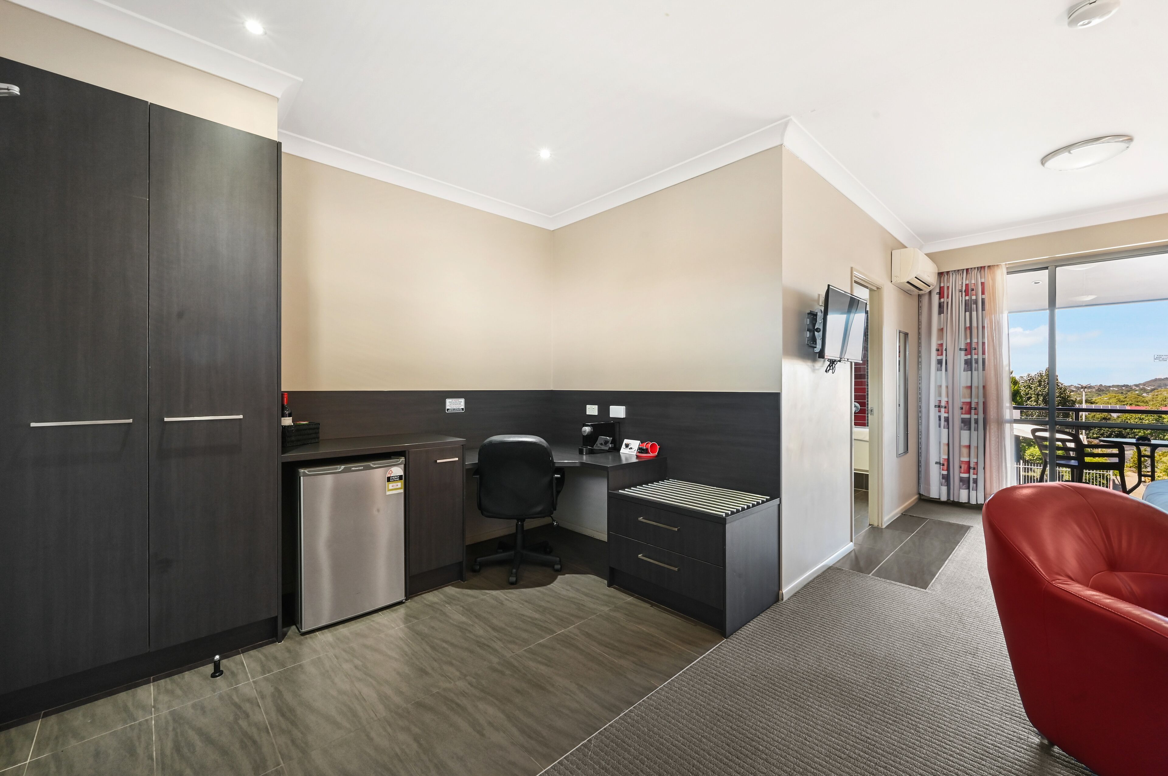 A modern kitchen with dark cabinetry, a small refrigerator, and a black office chair.