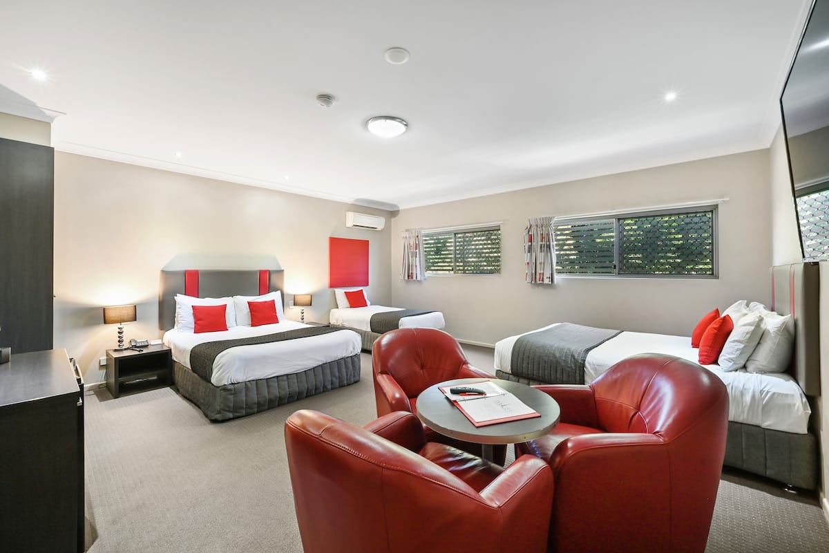 Una habitación de hotel con dos camas, un sofá de cuero rojo, una mesita redonda y un televisor.