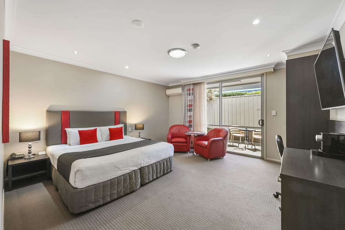 Habitación de hotel con una cama grande, un escritorio, dos sillas rojas y un balcón con vistas.