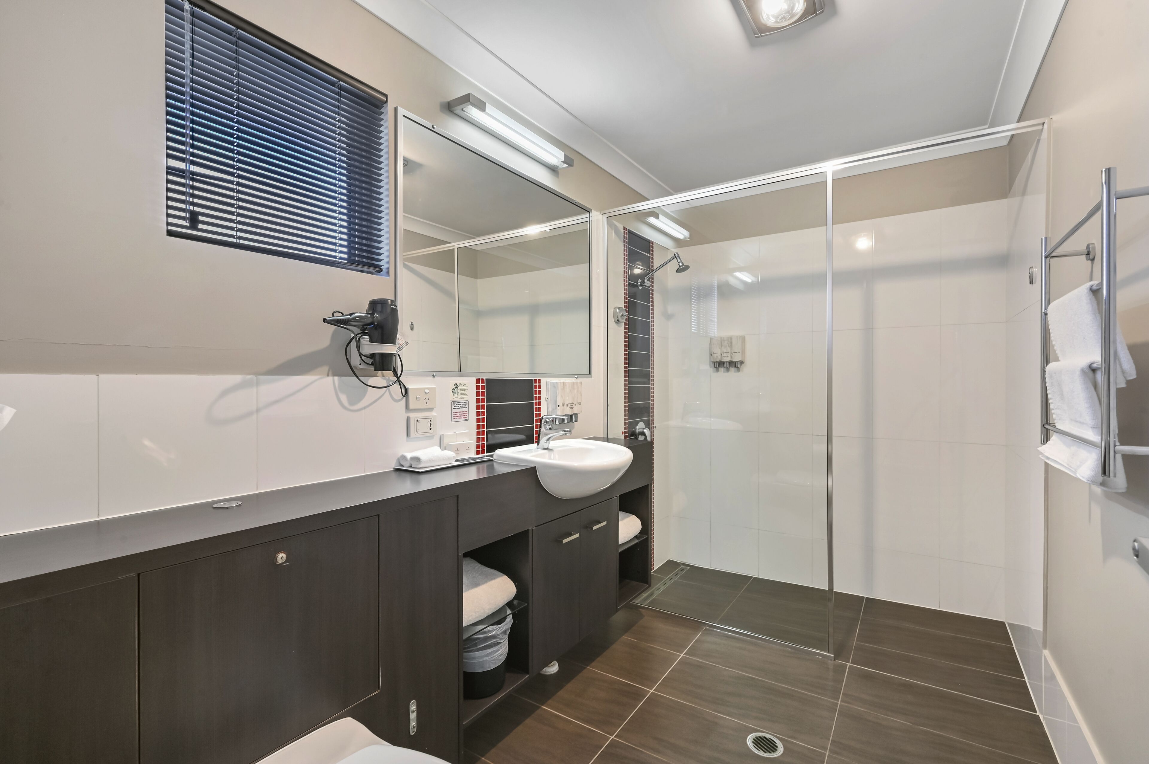 Une salle de bain moderne avec un meuble-lavabo en bois foncé, un lavabo blanc et une douche à parois de verre.