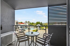 A balcony with a table and chairs, overlooking a parking area and buildings. - Platinum International (Harristown)