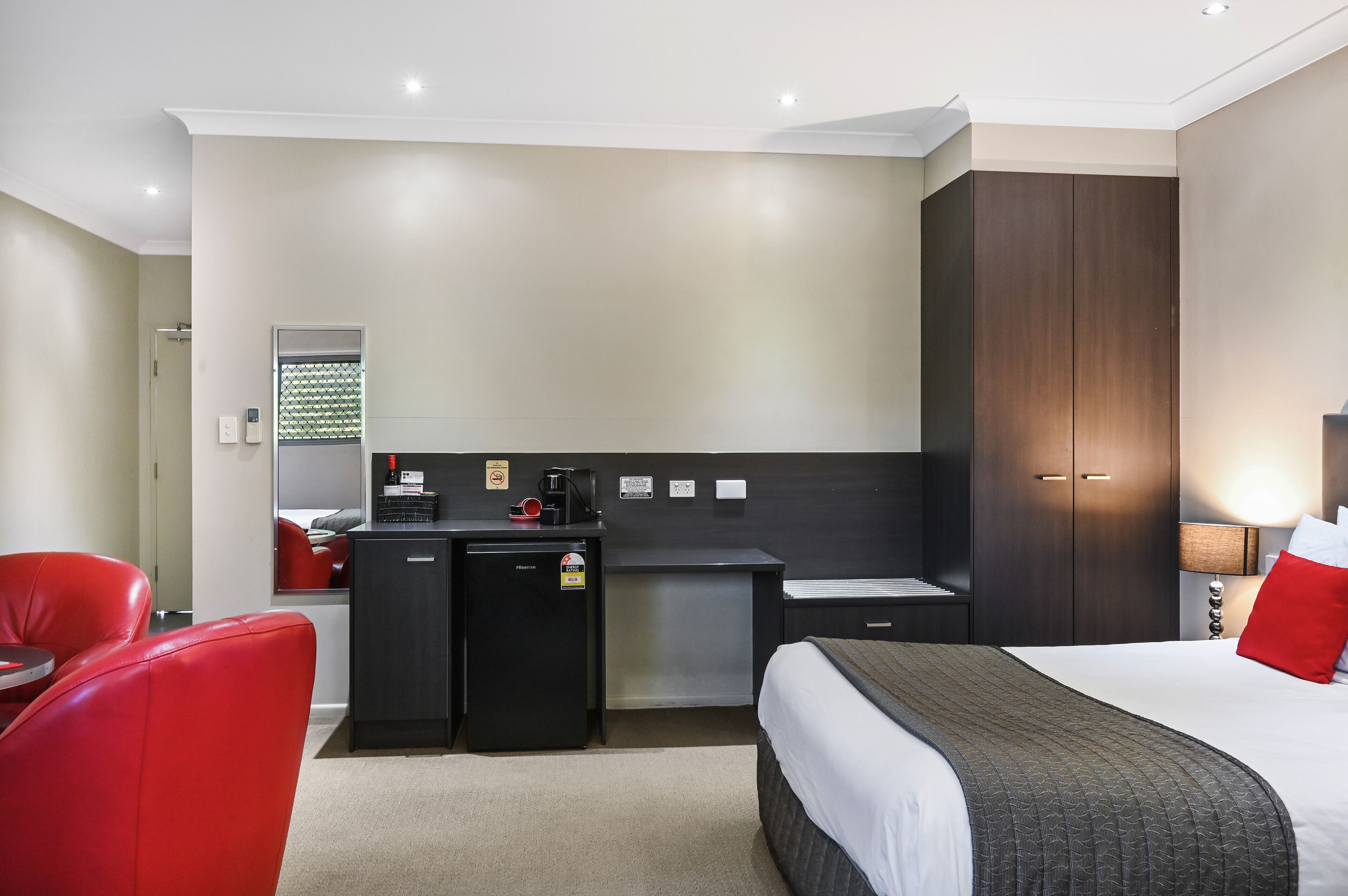 A hotel room with a bed, a desk, a chair, a small refrigerator, and a wardrobe.