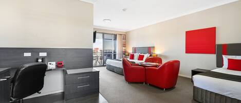 A modern hotel room with a desk, office chair, and a bed with red accents.