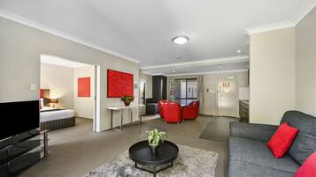A modern living room with a flat-screen TV, a sofa, a coffee table with a plant, and red chairs.