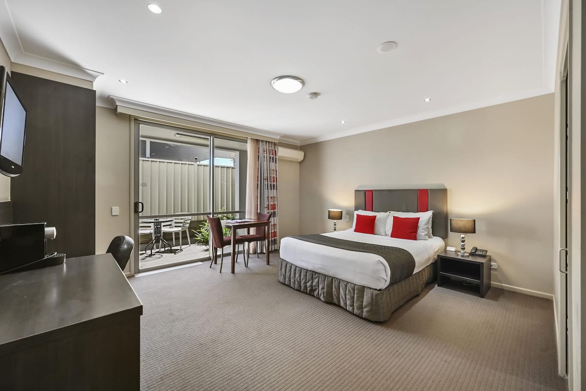 Una habitación de hotel con cama, mesita de noche, lámpara y escritorio con silla.