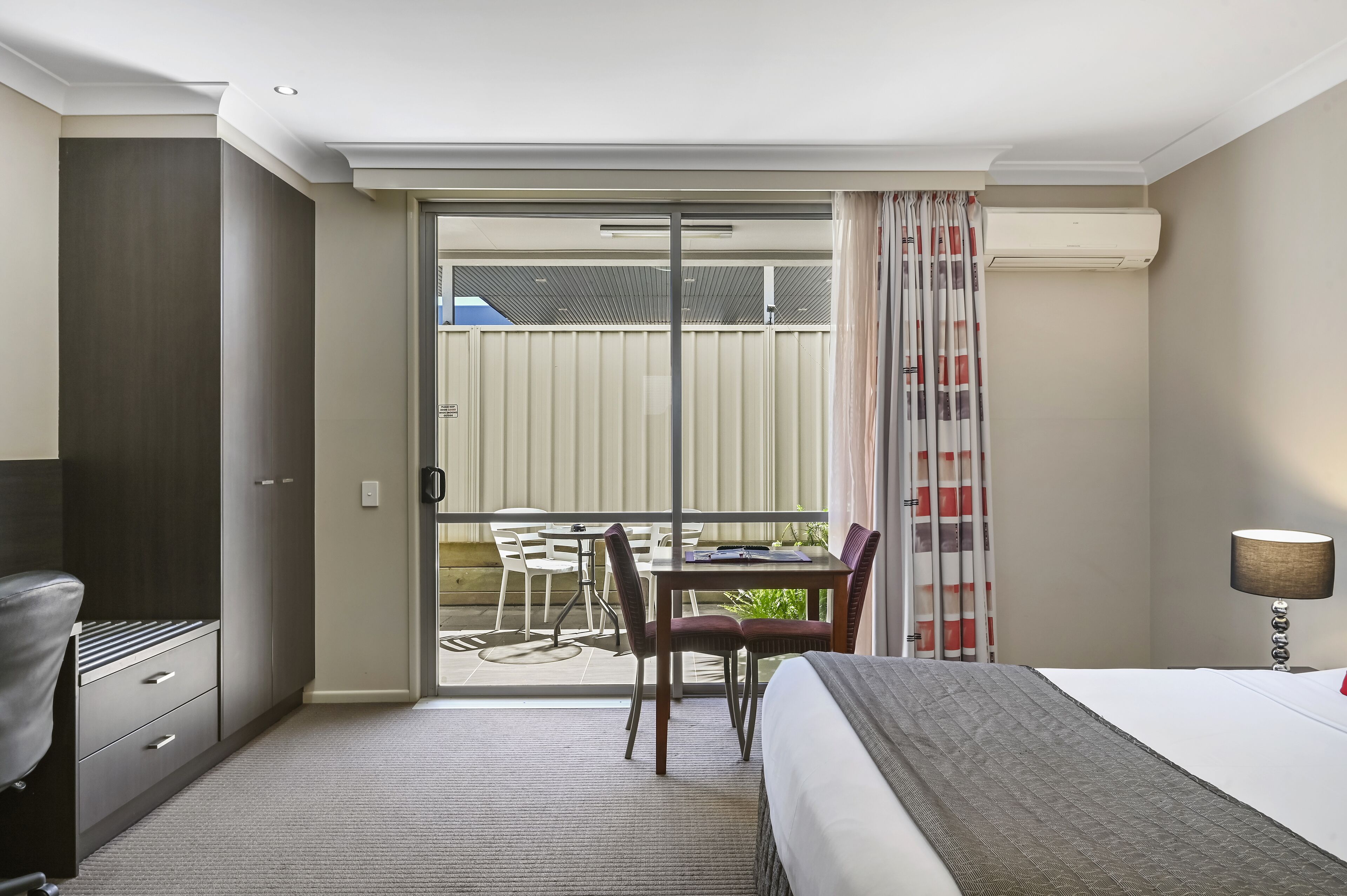 Een hotelkamer met een bed, een bureau en een stoel. Er is een balkon met een tafel en stoelen.