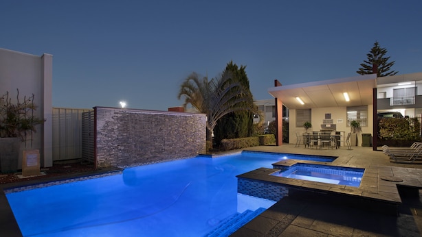 Piscina con muro de piedra y zona de patio con mobiliario exterior.