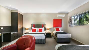 A hotel room with two beds, a red chair, a desk, and a wardrobe.