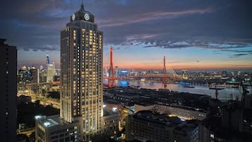 A high-rise building with a prominent clock tower, situated in a cityscape with a river and a bridge in the background.