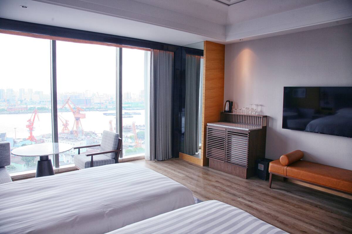 Una habitación de hotel con un ventanal grande, una cama, un escritorio y un televisor.