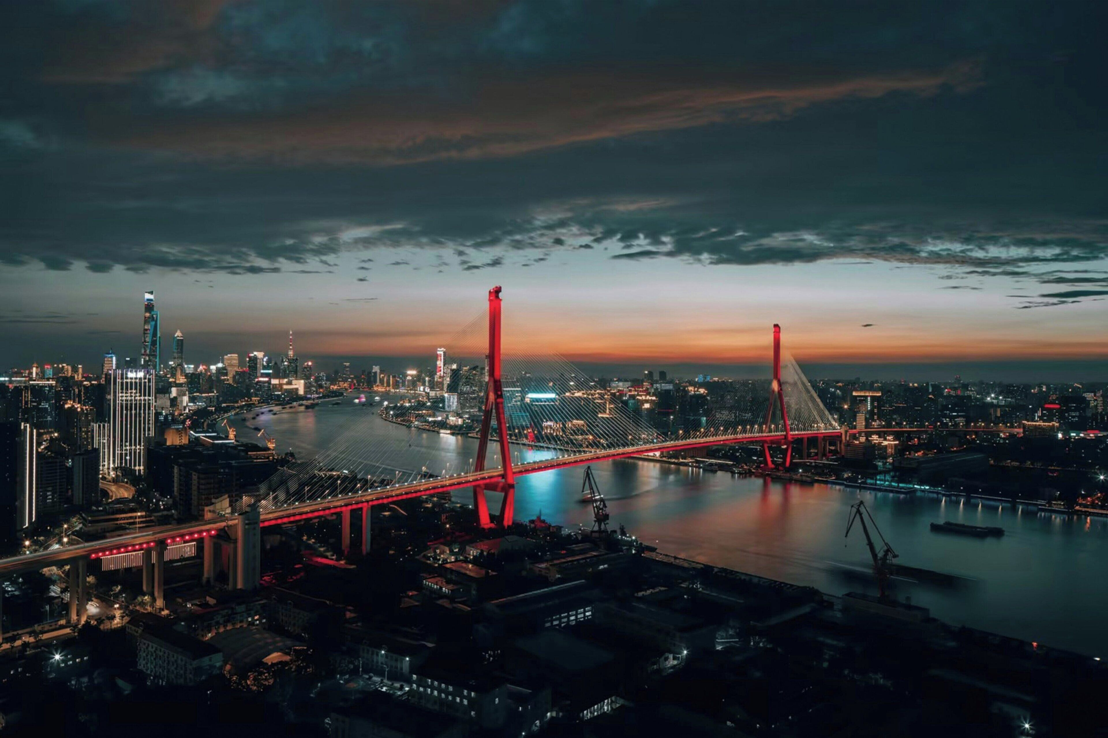 Un paisaje urbano al atardecer con un puente rojo destacado cruzando un río.