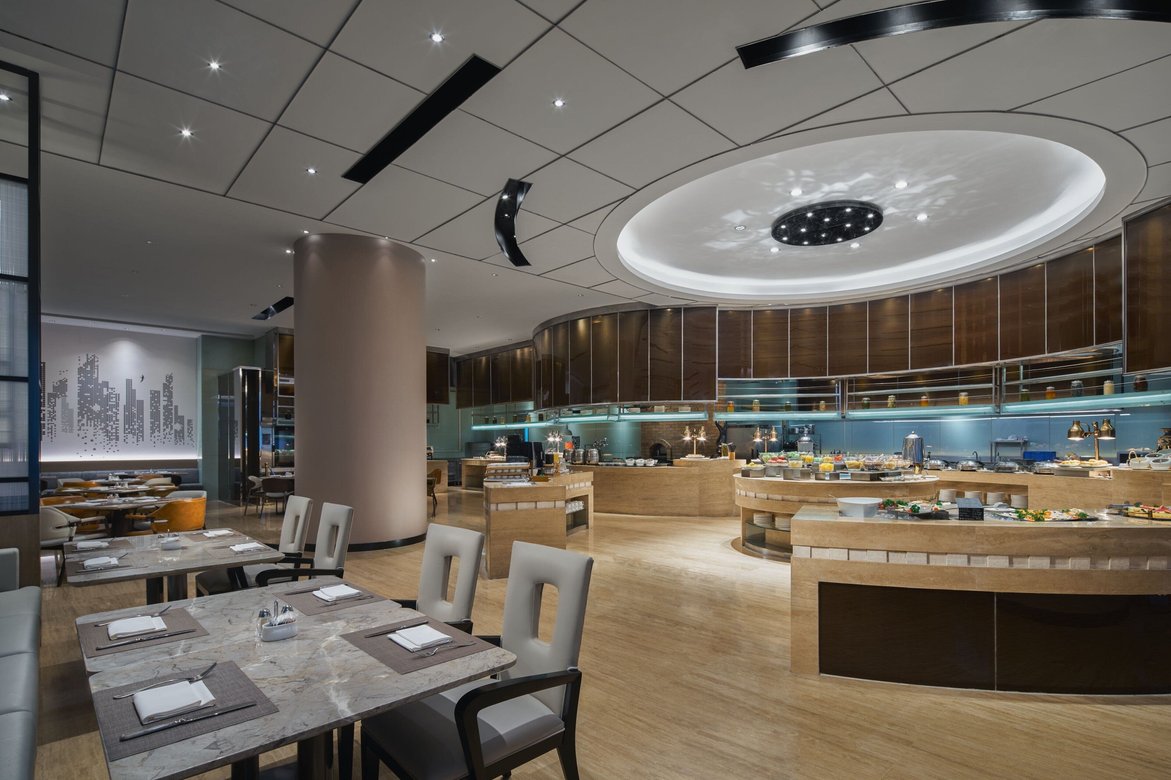 A modern hotel lobby with a central reception desk, seating area, and a cityscape mural on the wall.