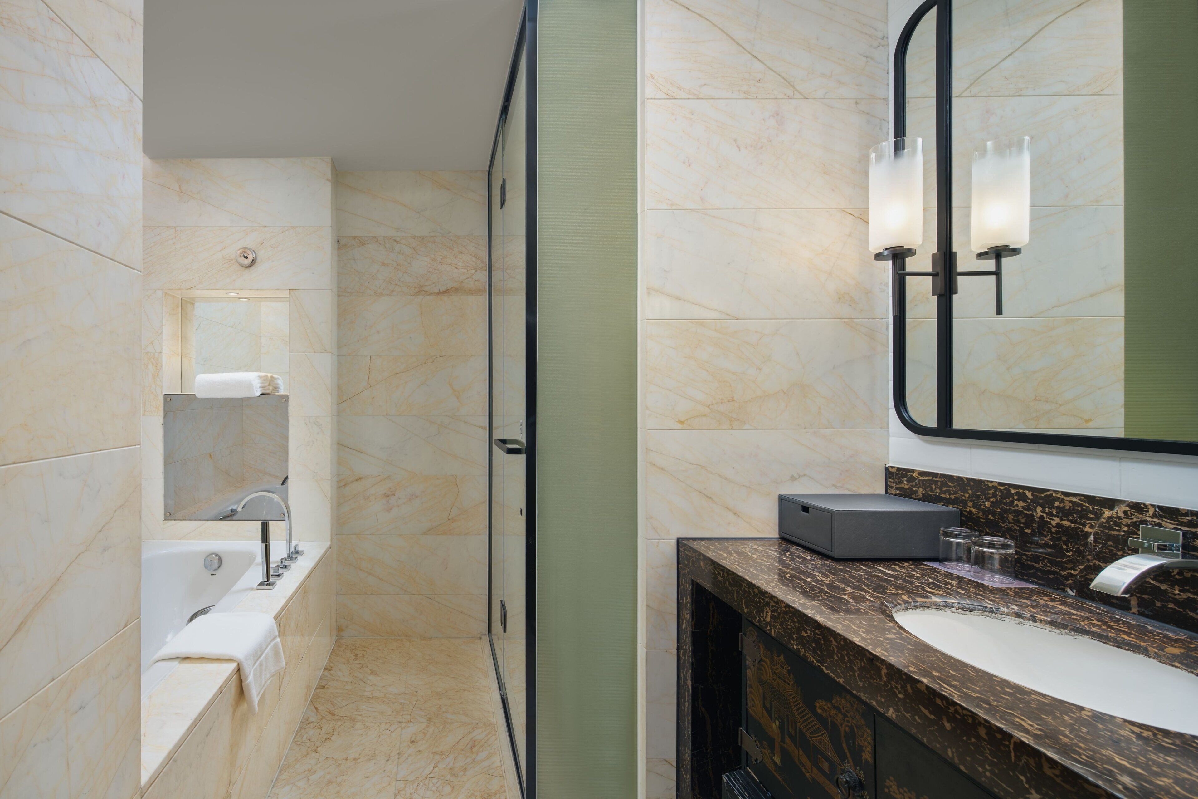 A modern bathroom with a marble floor, a bathtub, a sink with a marble countertop, and a large mirror.