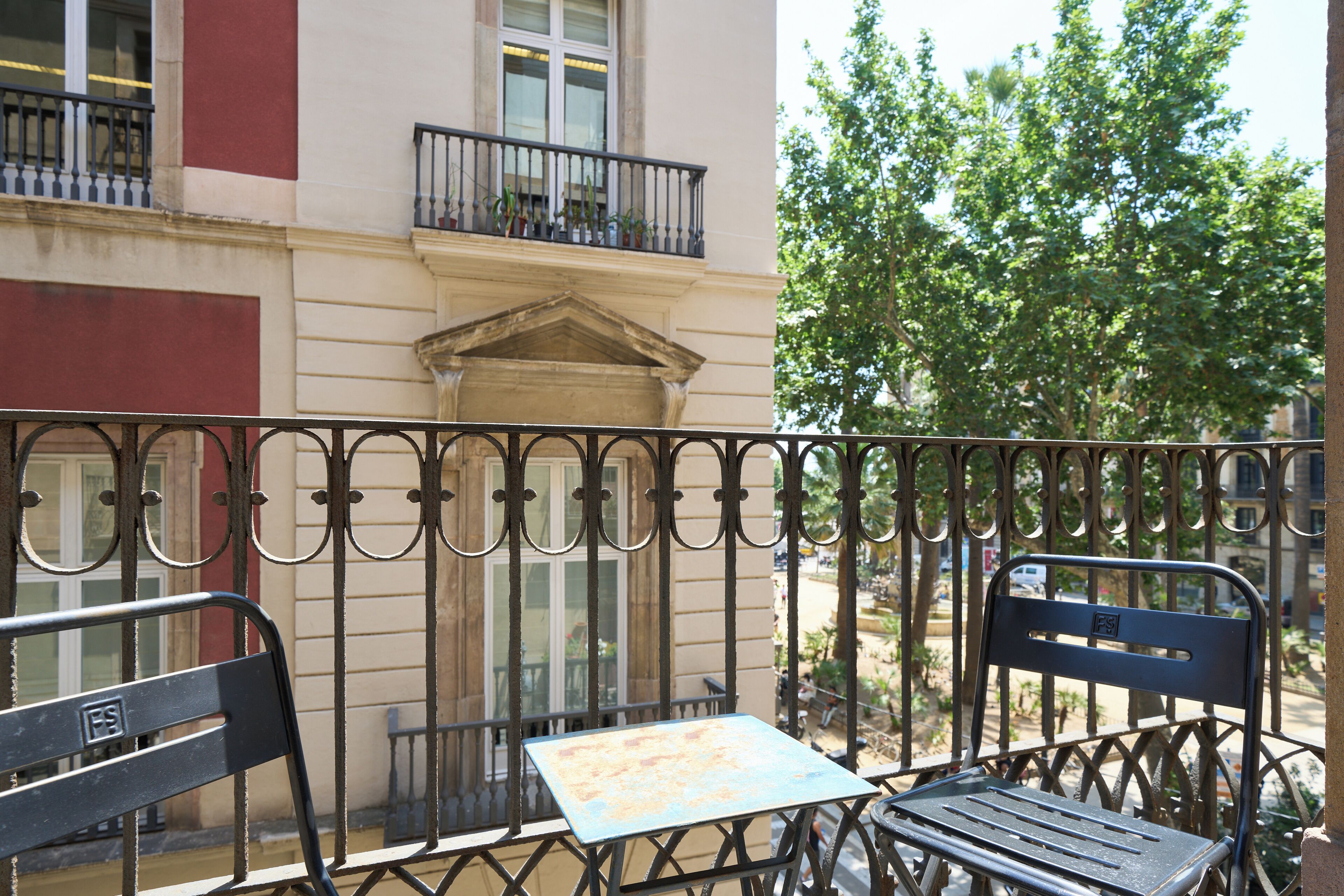 Een balkon met een metalen hekwerk, een tafel en twee stoelen.
