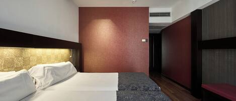 Ein Hotelzimmer mit Bett, Sitzbank, einem gemusterten Teppich und einer roten Akzentwand.