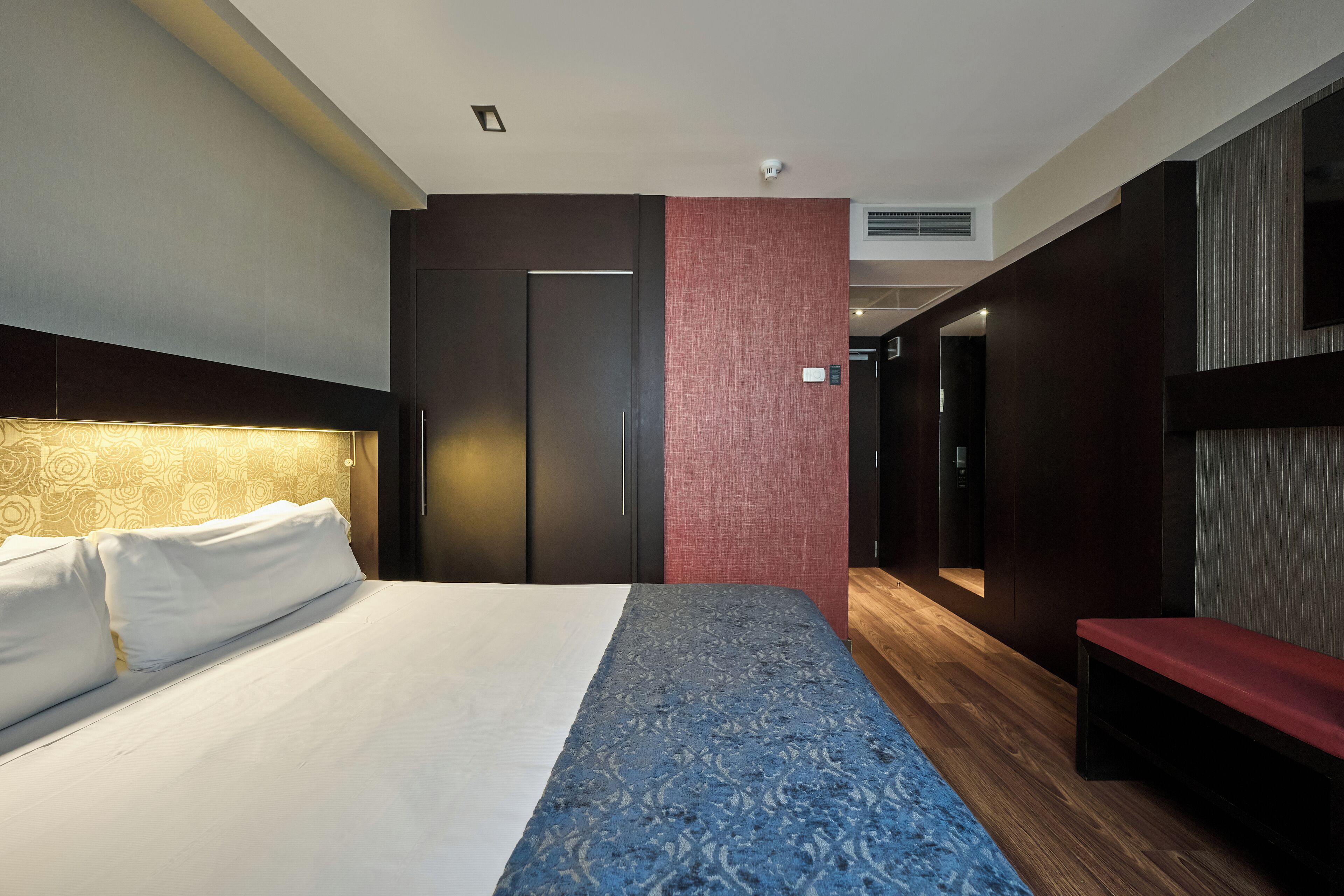 Una habitación de hotel moderna con una cama grande, un banco y un armario.