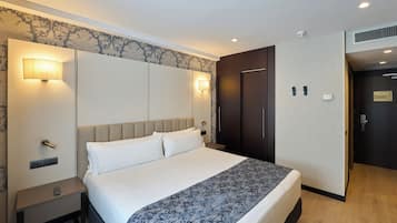 A hotel room with a bed, nightstands, wall sconces, a wardrobe, and a door with a sign.