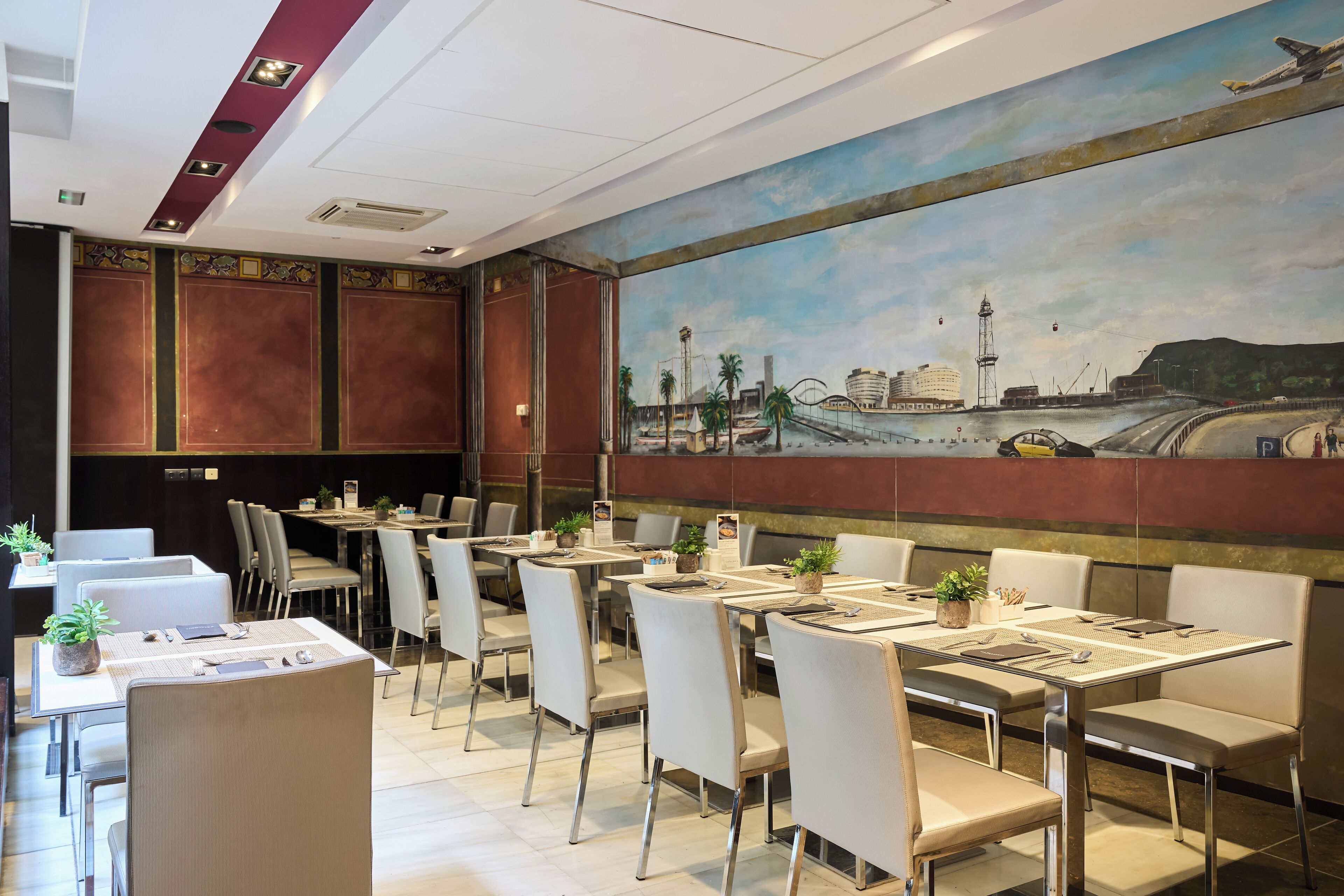 A restaurant with multiple tables and chairs, a mural on the wall depicting a cityscape, and a ceiling with recessed lighting.