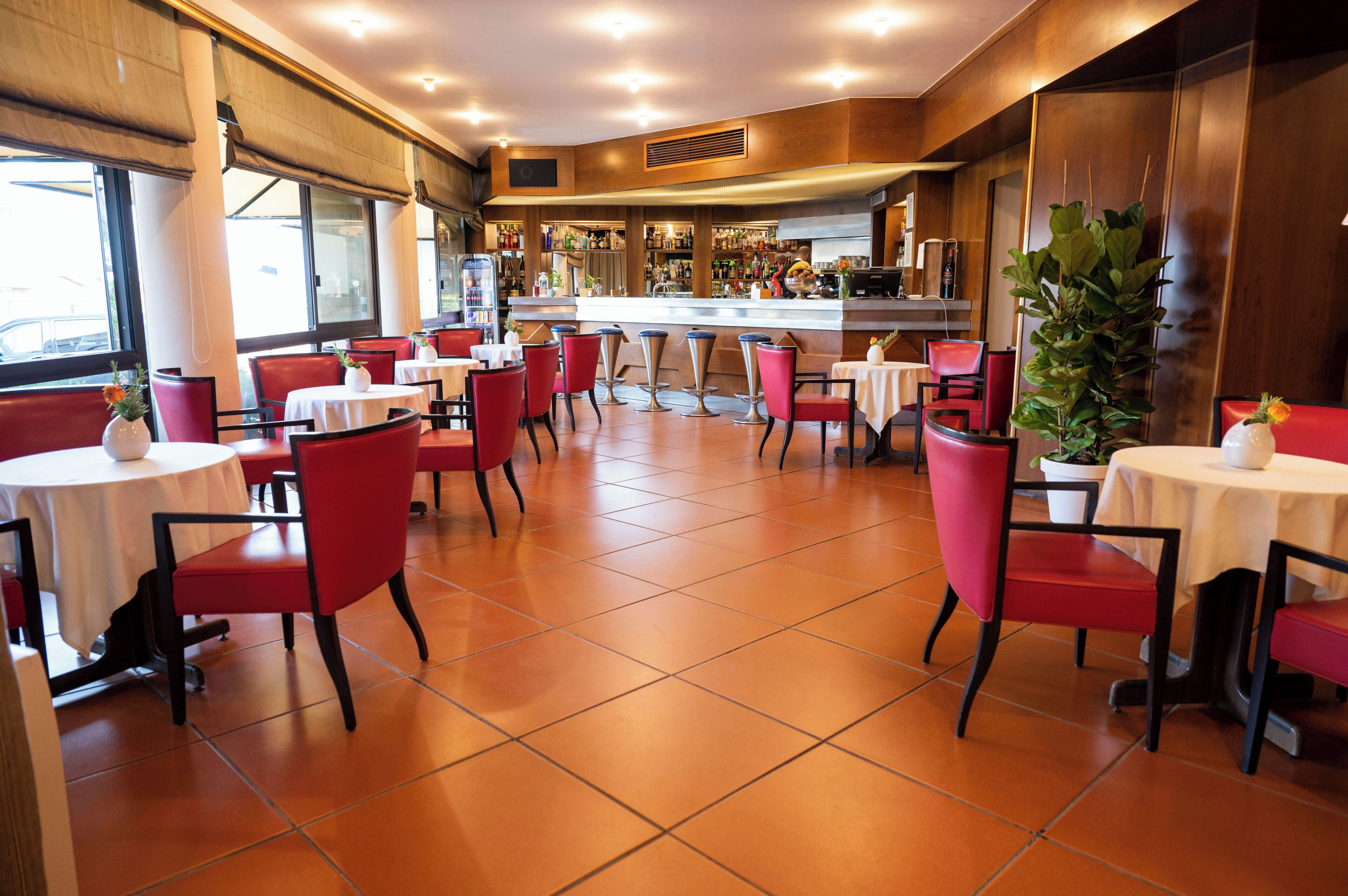 Ein Restaurantinneres mit roten Stühlen, weißen Tischen, einer Bar und einer großen Pflanze in einem Topf.