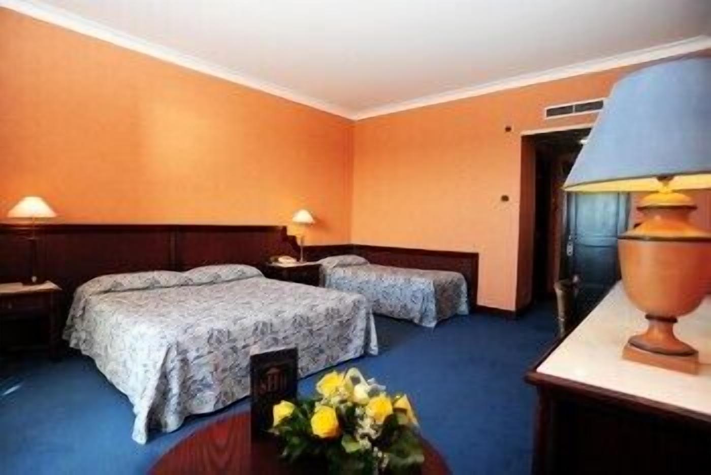 A hotel room with two beds, a nightstand, a lamp, and a vase with flowers.