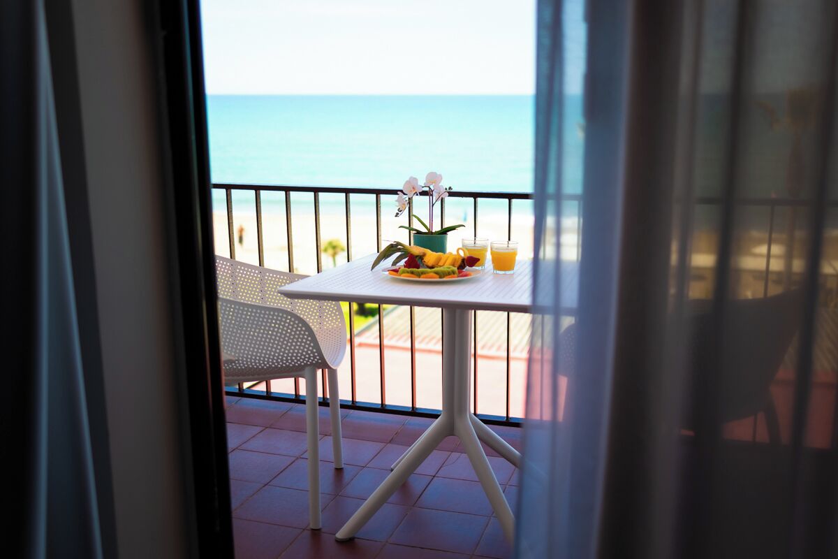 Un balcón con una mesa para dos, una silla y vista a la playa.
