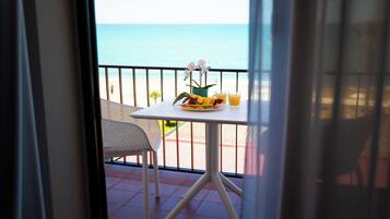 Un balcón con una mesa para dos, una silla y vista a la playa.