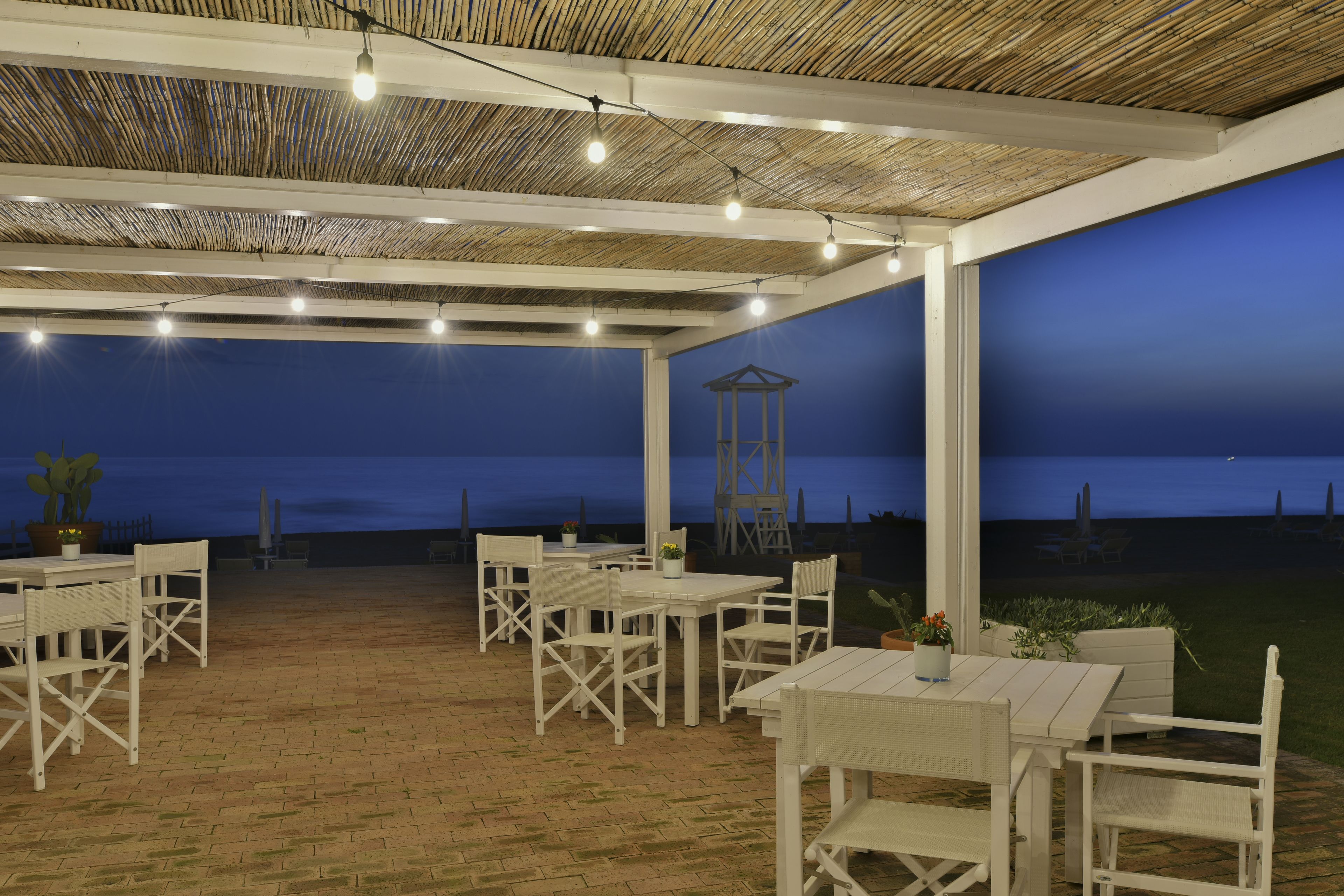 An outdoor patio with white furniture and a thatched roof.