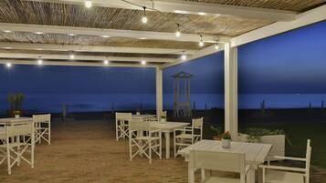 An outdoor patio with white furniture and a thatched roof.