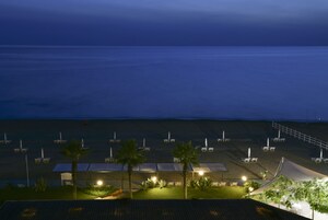 A beachside hotel with rows of sun loungers and umbrellas, a covered seating area, and a view of the ocean.