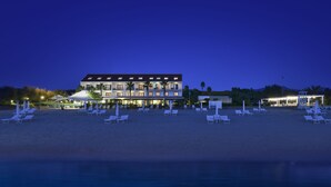 Un hôtel situé en bord de mer, doté de nombreux balcons, d’un espace piscine et de chaises longues sur la plage.