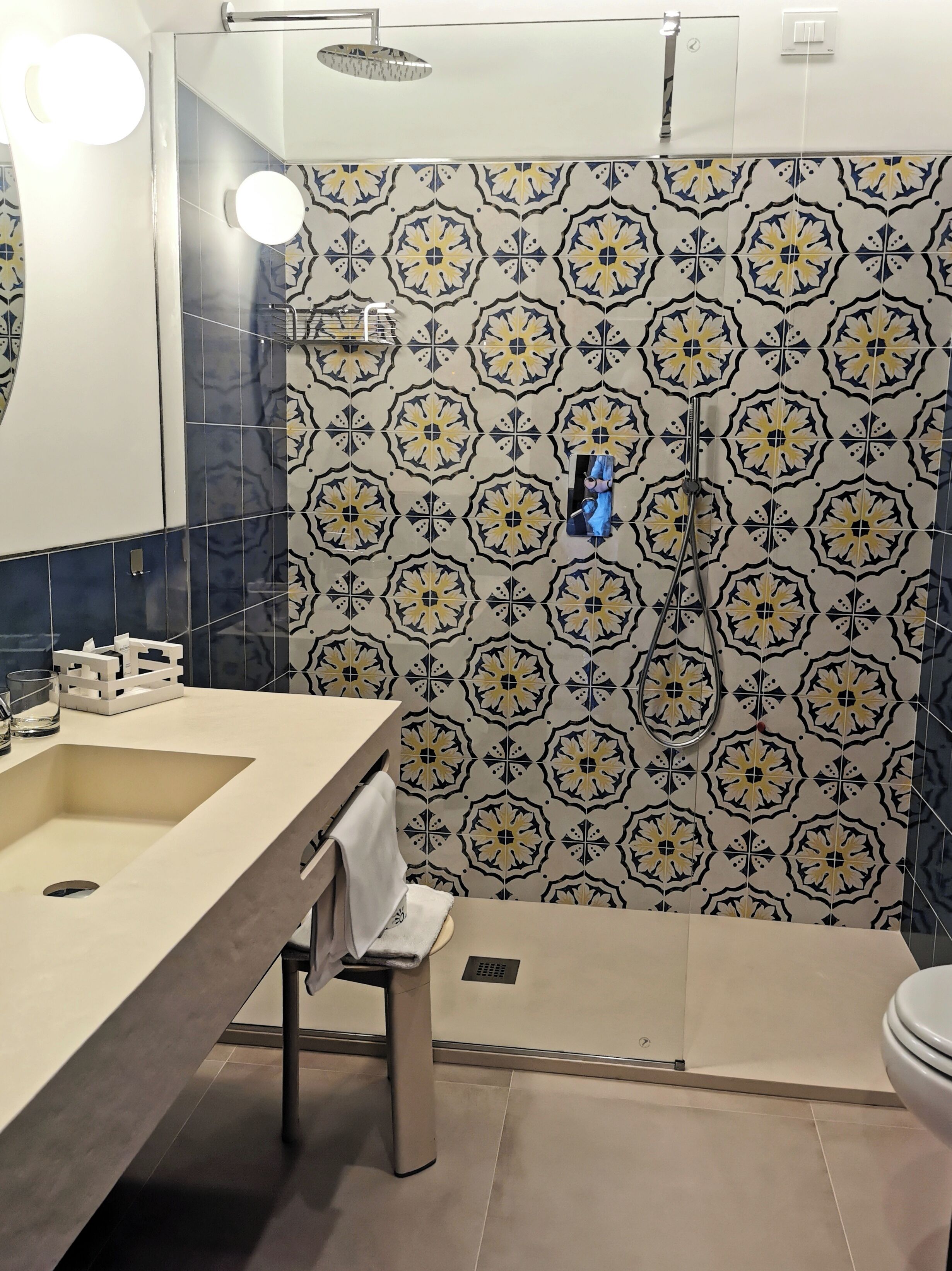 A bathroom with a sink, mirror, towel rack, shower, and patterned tiles.