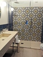 A bathroom with a sink, mirror, towel rack, shower, and patterned tiles.