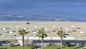 Une plage avec des parasols blancs et des chaises longues, un palmier et une vue dégagée sur l’océan.