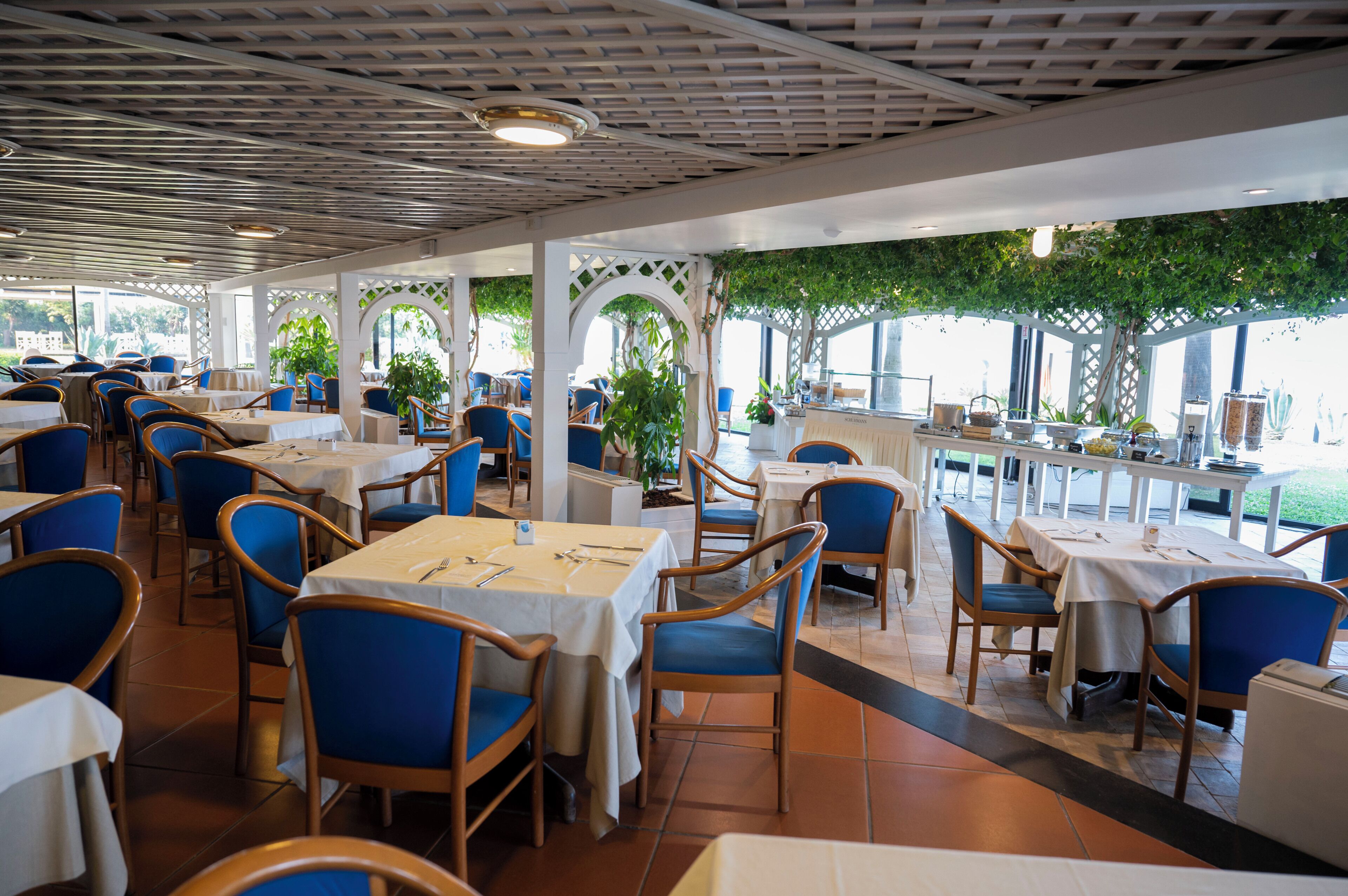 Un restaurante con terraza, mesas blancas, sillas azules y vistas al mar.